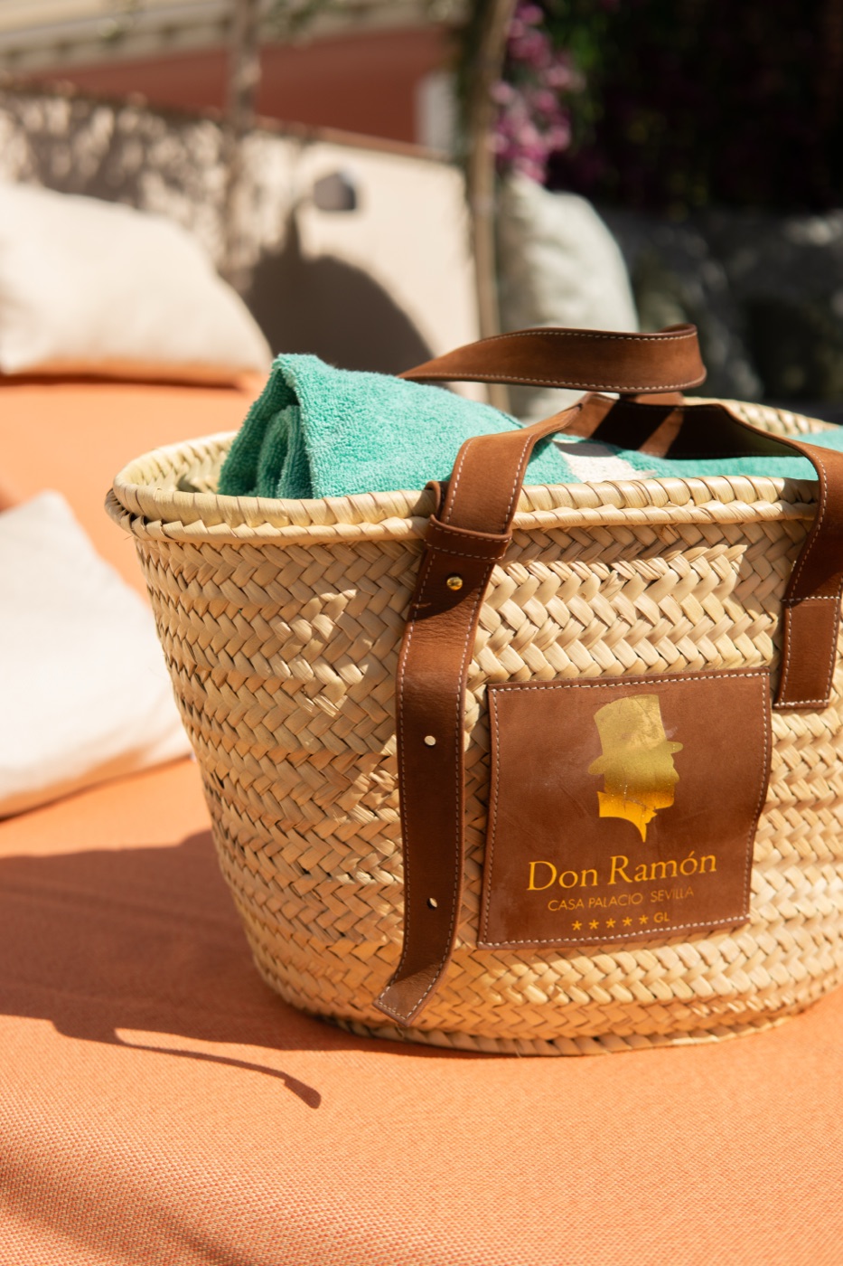 Straw basket with towels and a Don Ramón leather tag beside the pool